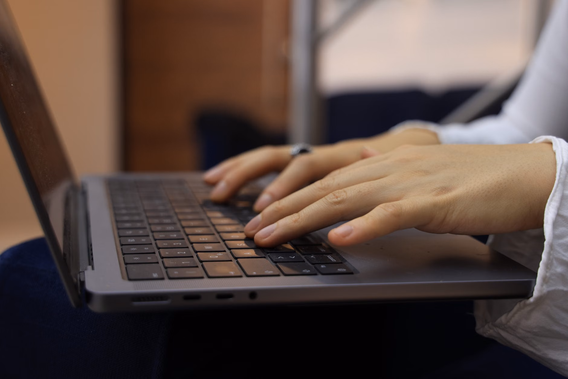 Mani che digitano sulla tastiera di un portatile in un ambiente interno. Perfetto per temi aziendali e tecnologici.