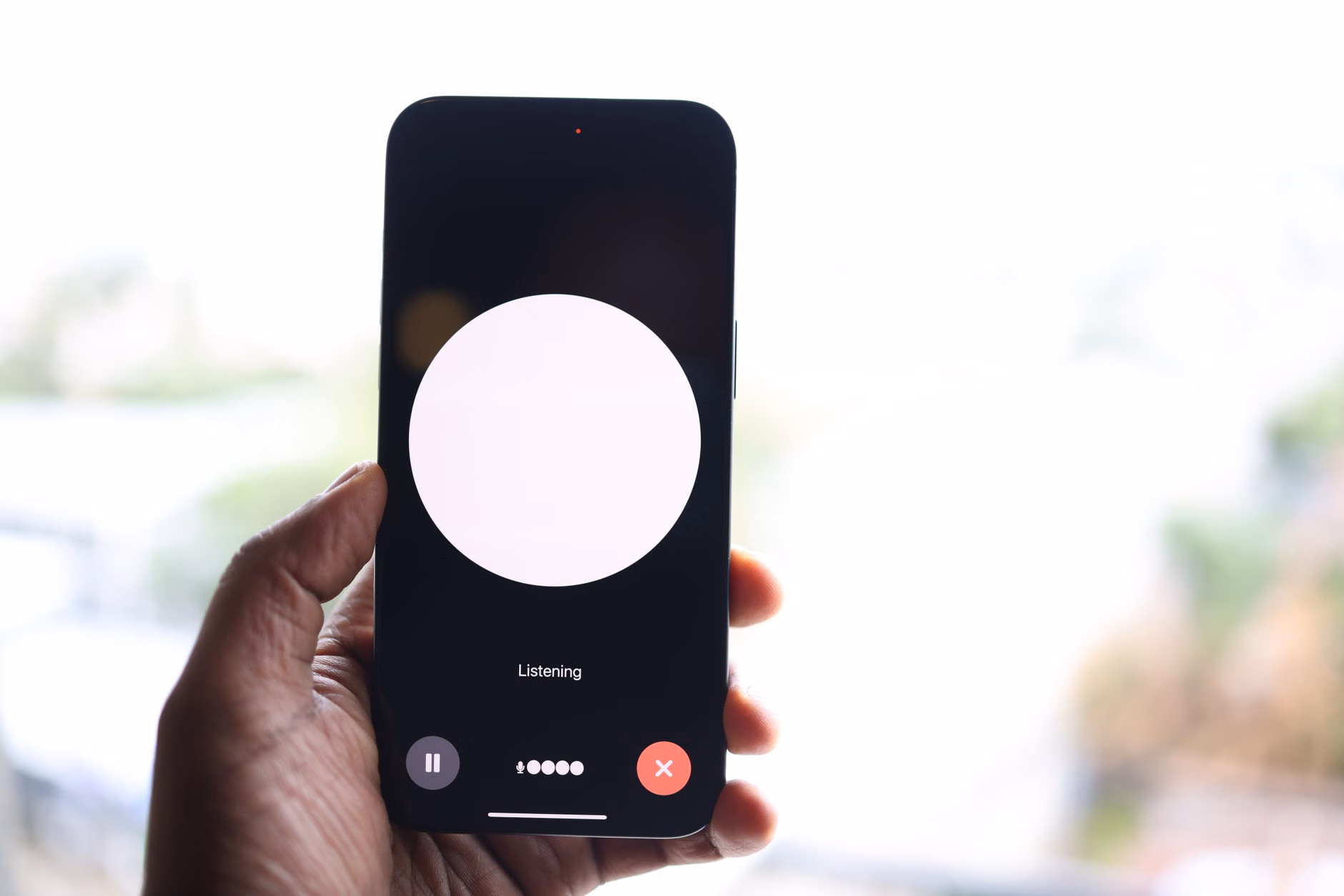 Primo piano di una mano che tiene uno smartphone con l'interfaccia di un assistente vocale.