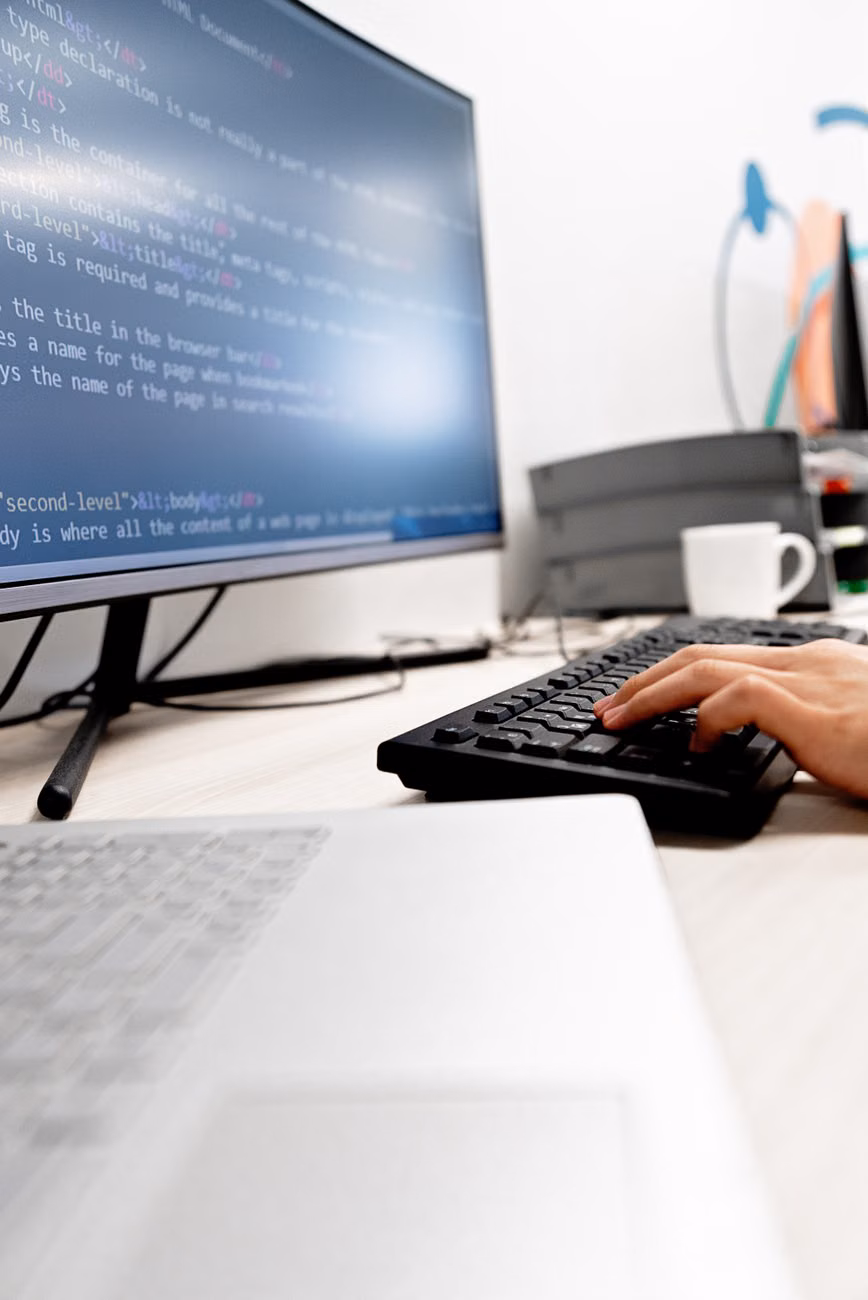 Close-up of hands typing code on a computer monitor in an office setting.