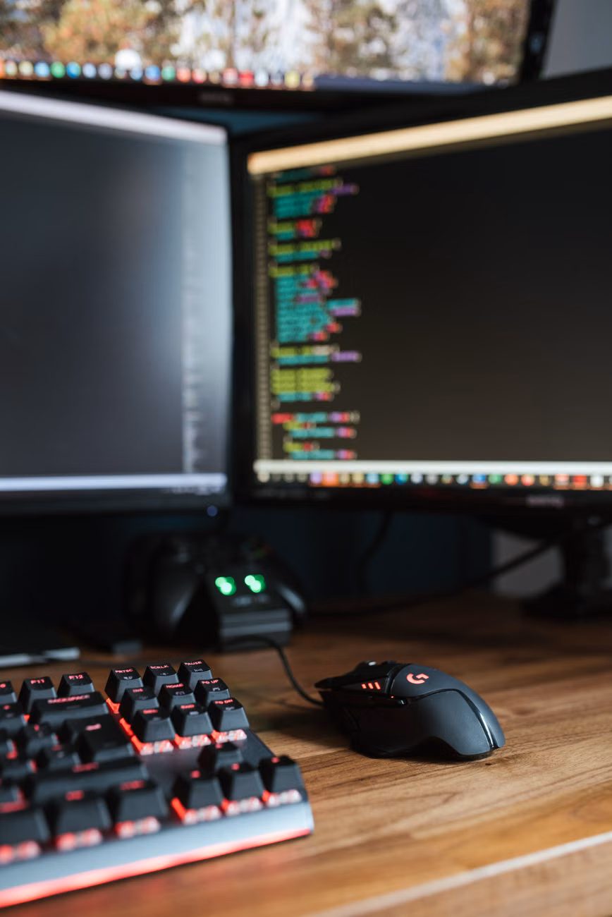 Modern computer monitors with programming code placed on desk with keyboard and mouse.
